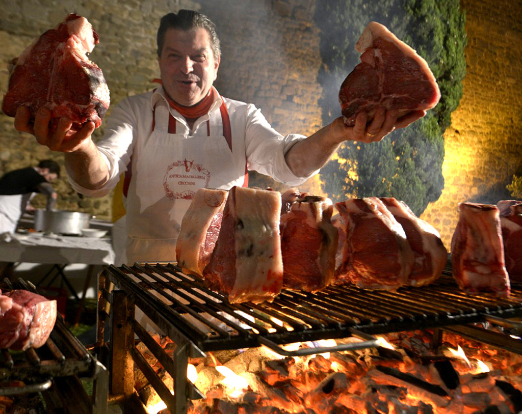 Dario Cecchini in front of charcoal grill with T-bone steaks